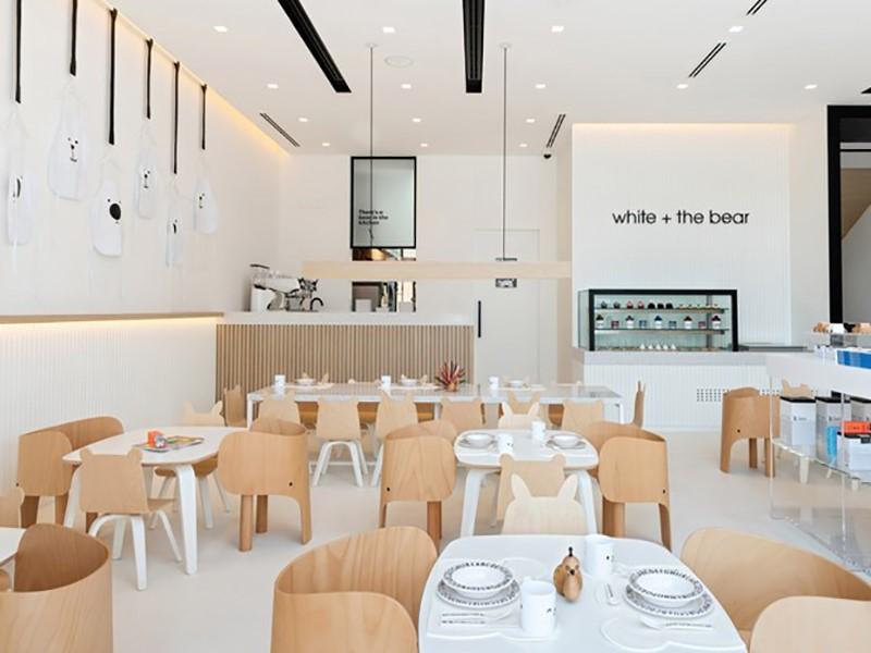 Restaurante infantil tem superfícies brancas e móveis de madeira